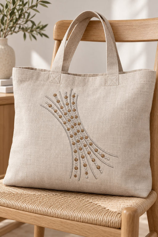 Photorealistic sweeping seed dot branch machine embroidery in soft graphite and warm bronze thread on a linen tote bag, shown as one fabric-stitched motif