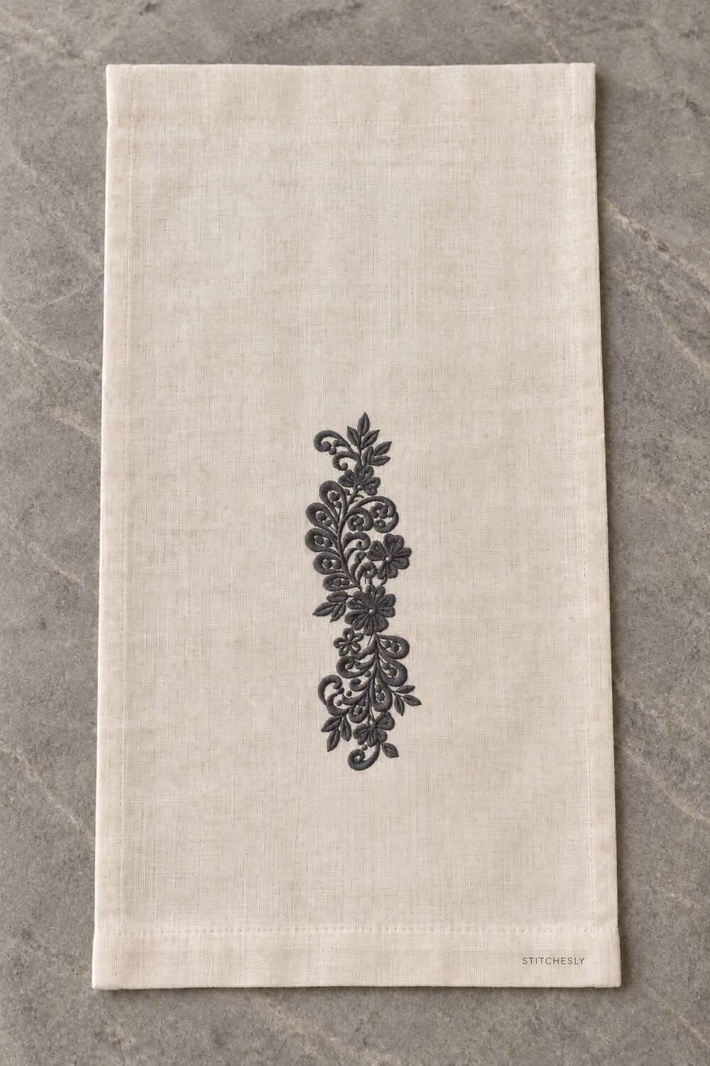 Generated usage mockup of a linen guest towel with the teardrop leaf floral vine machine embroidery motif in one soft deep graphite charcoal thread color.