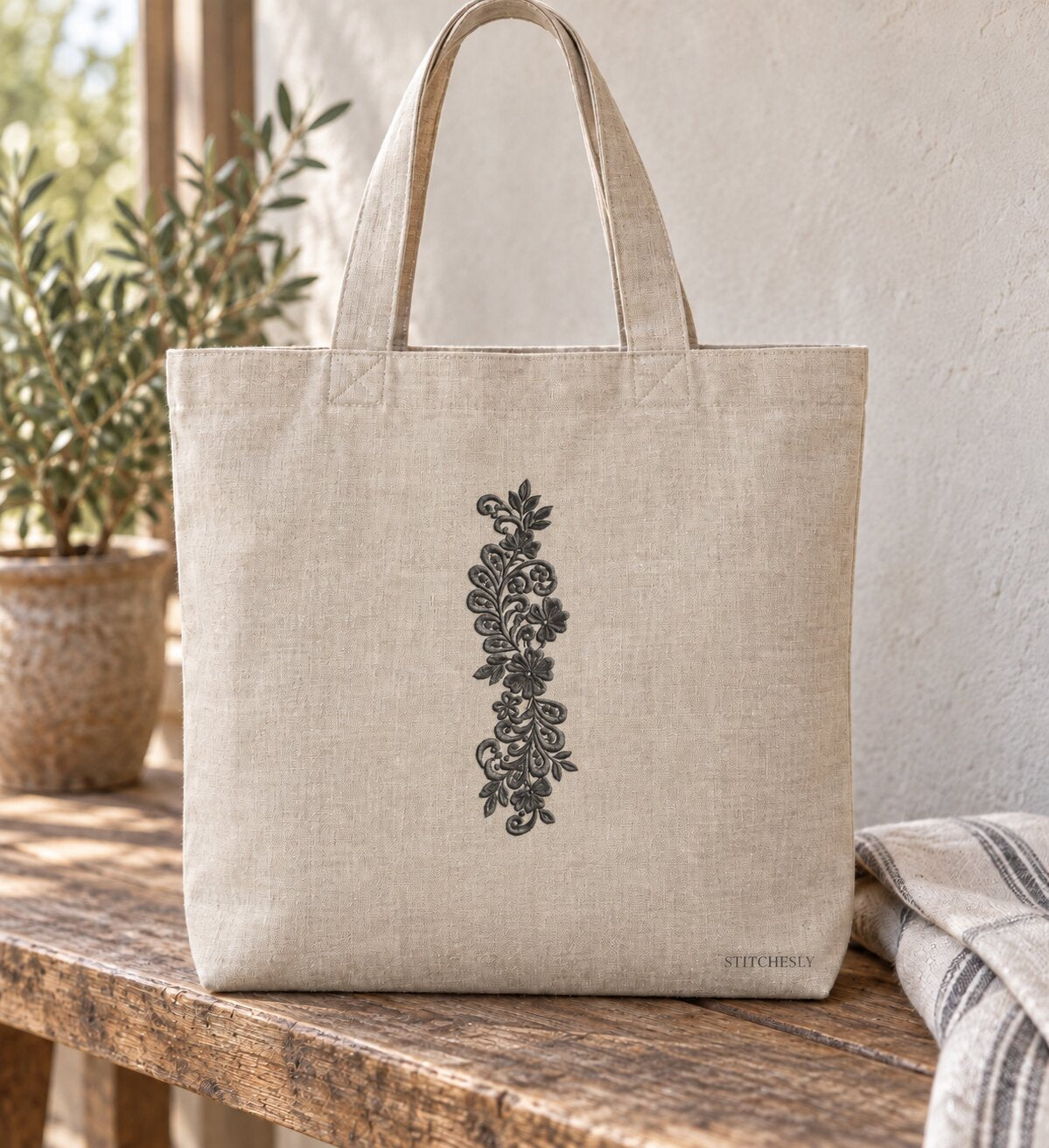 Generated usage mockup of a linen tote bag with the teardrop leaf floral vine machine embroidery motif in one soft deep graphite charcoal thread color.