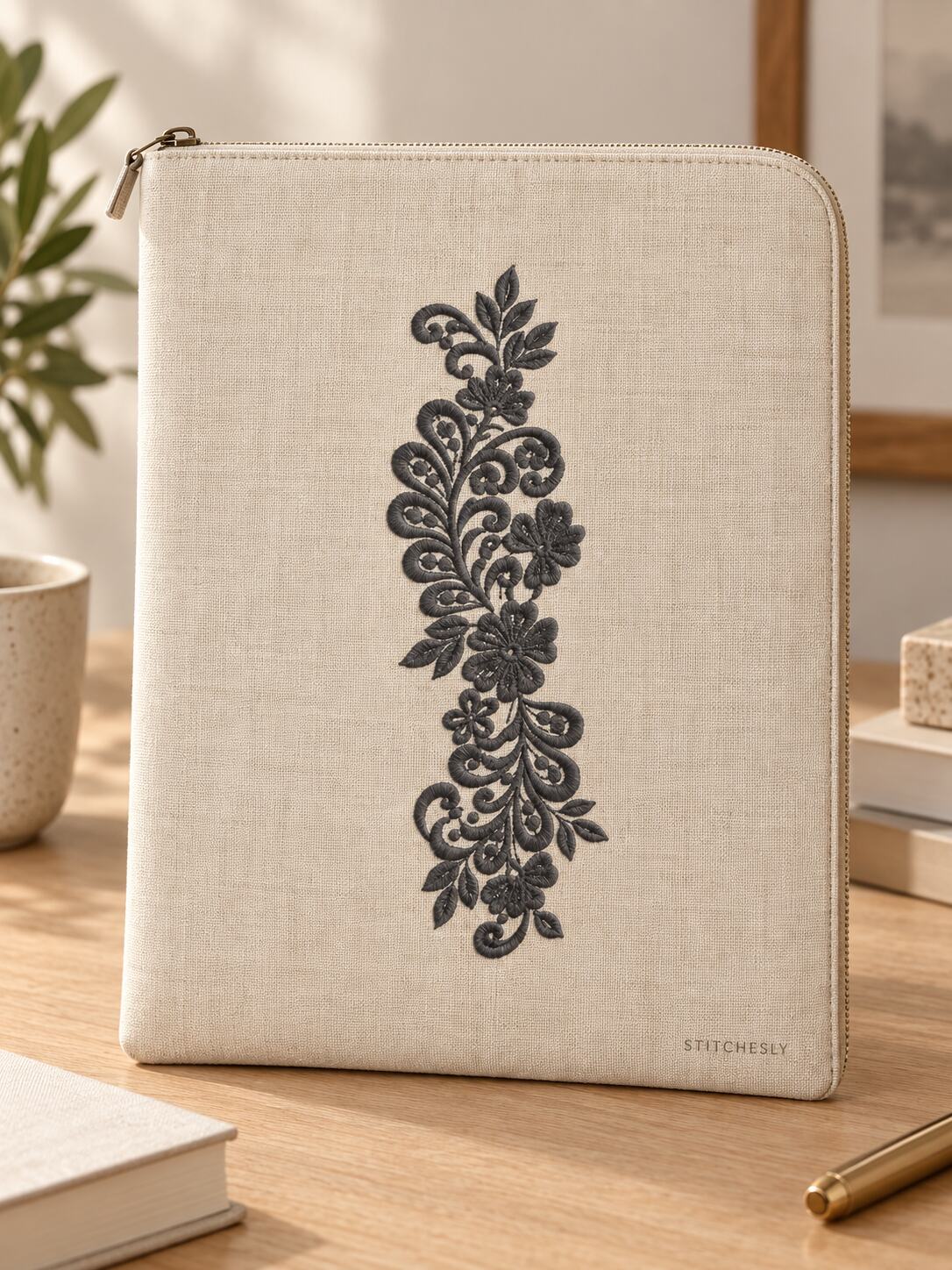 Generated usage mockup of a linen zip folio with the teardrop leaf floral vine machine embroidery motif in one soft deep graphite charcoal thread color.