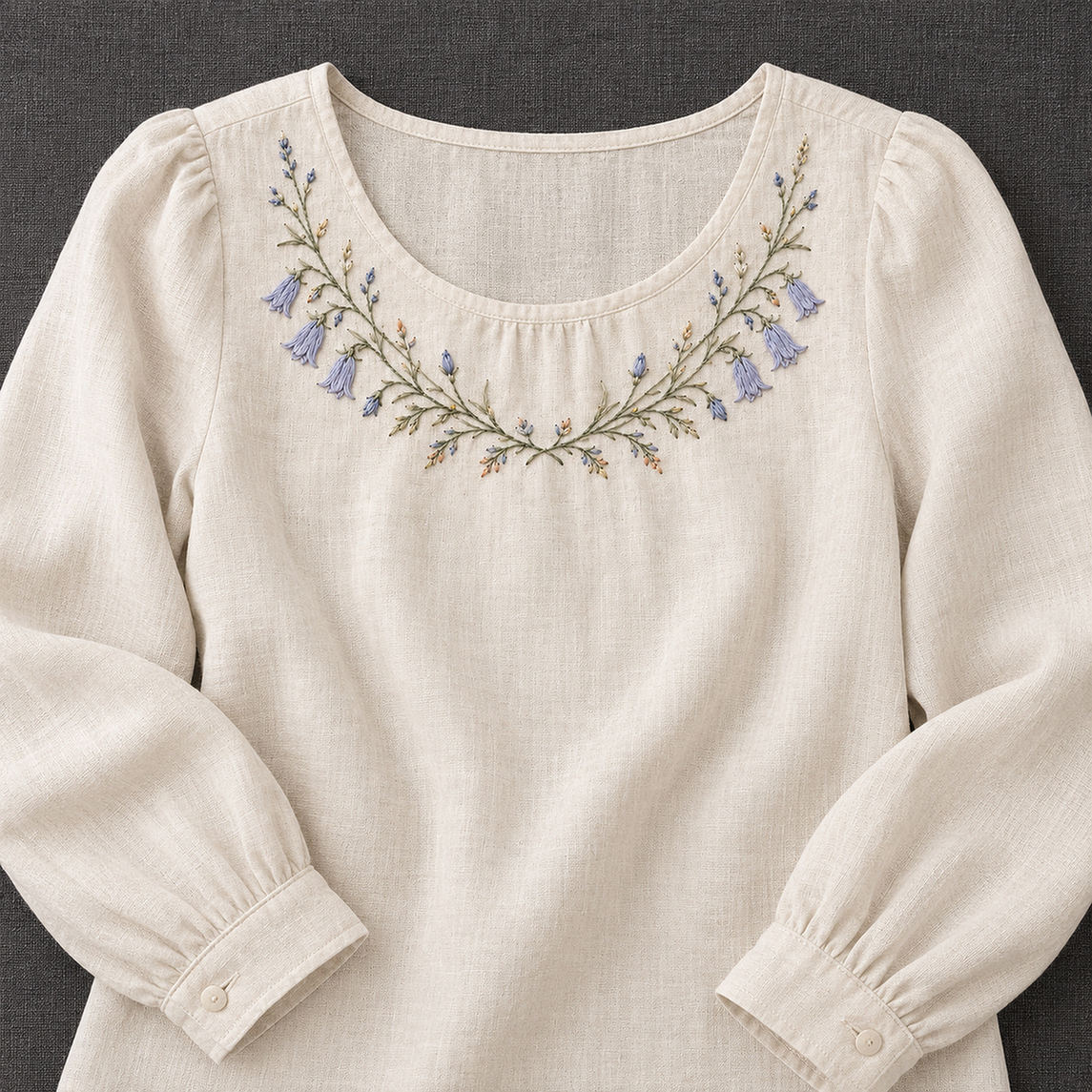 Linen blouse mockup featuring the Harebell Collar Arc hand embroidery design. Blue harebells, buds and fine foliage follow a shallow collar arc.