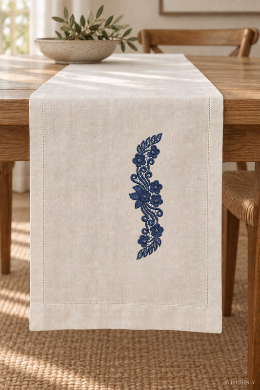 Generated usage mockup of a linen table runner with the leaf capped floral scroll machine embroidery motif in one deep midnight indigo blue thread color.