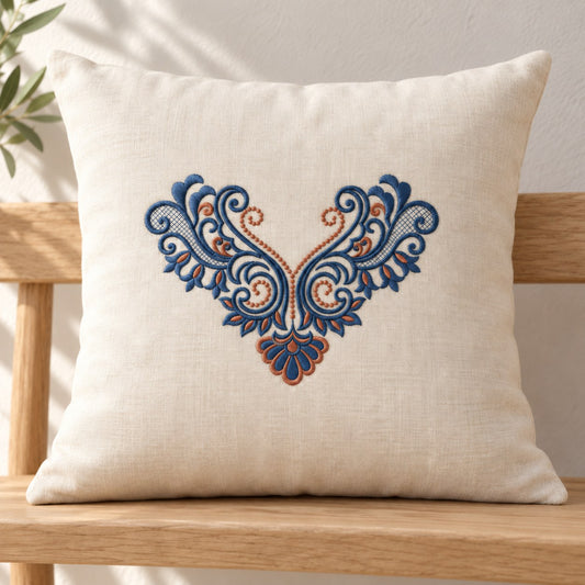 Ivory linen cushion with a centered ink-blue and copper acanthus V ornament, paired scrolls and a fan-shaped drop.