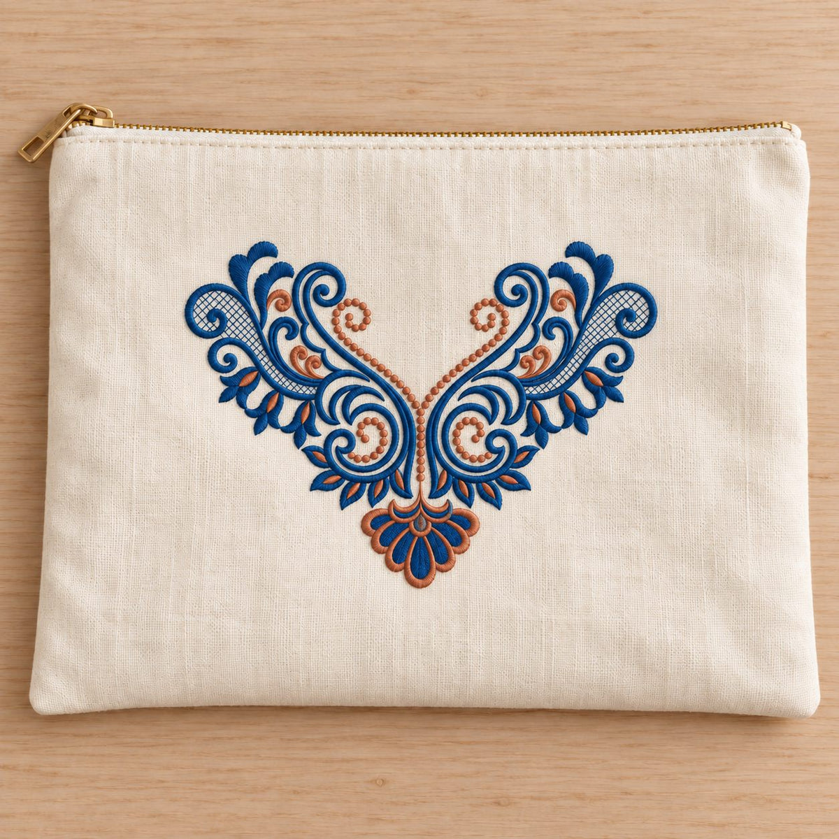 Ivory zippered linen folio with symmetrical blue scroll embroidery, copper leaf centers and a fan-shaped pendant.