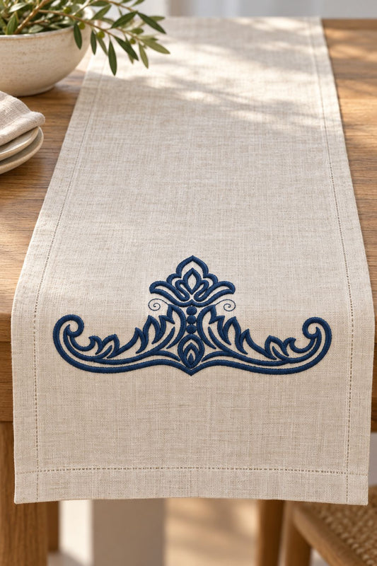 Photorealistic acanthus leaf crest machine embroidery in deep ink navy thread on a linen table runner, shown as one fabric-stitched motif