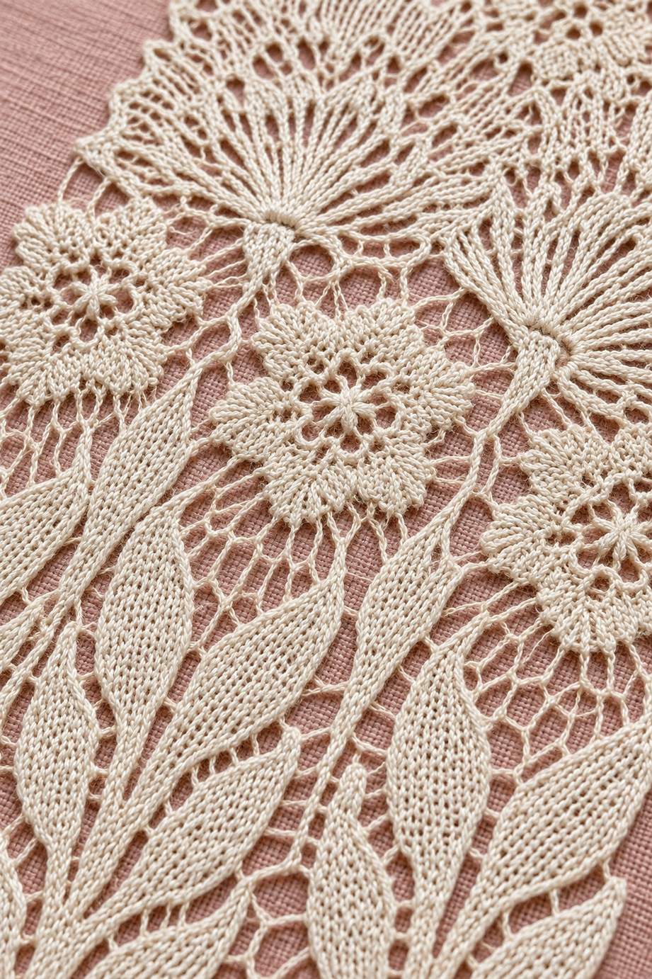 Warm ivory open-petal daisies, small rosettes and elongated leaves in a close needlelace panel on dusty rose linen.