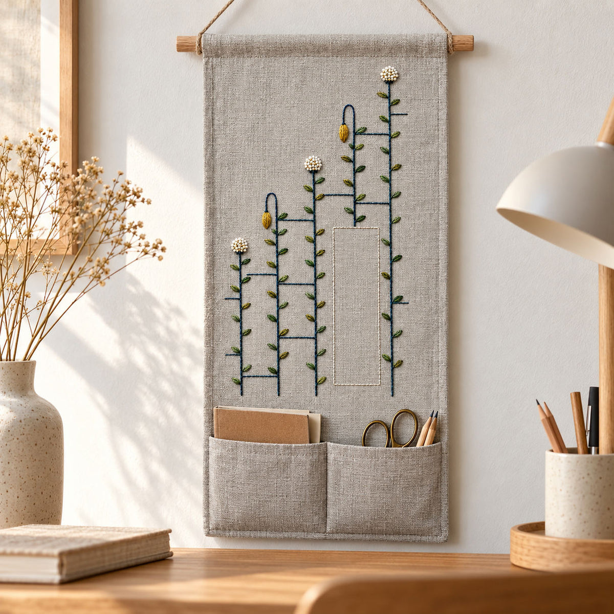 Framed textile by a window mockup featuring the Ladder Stem Meadow hand embroidery design. Meadow stems pass through interrupted ladder bars in this geometric hand embroidery pattern.