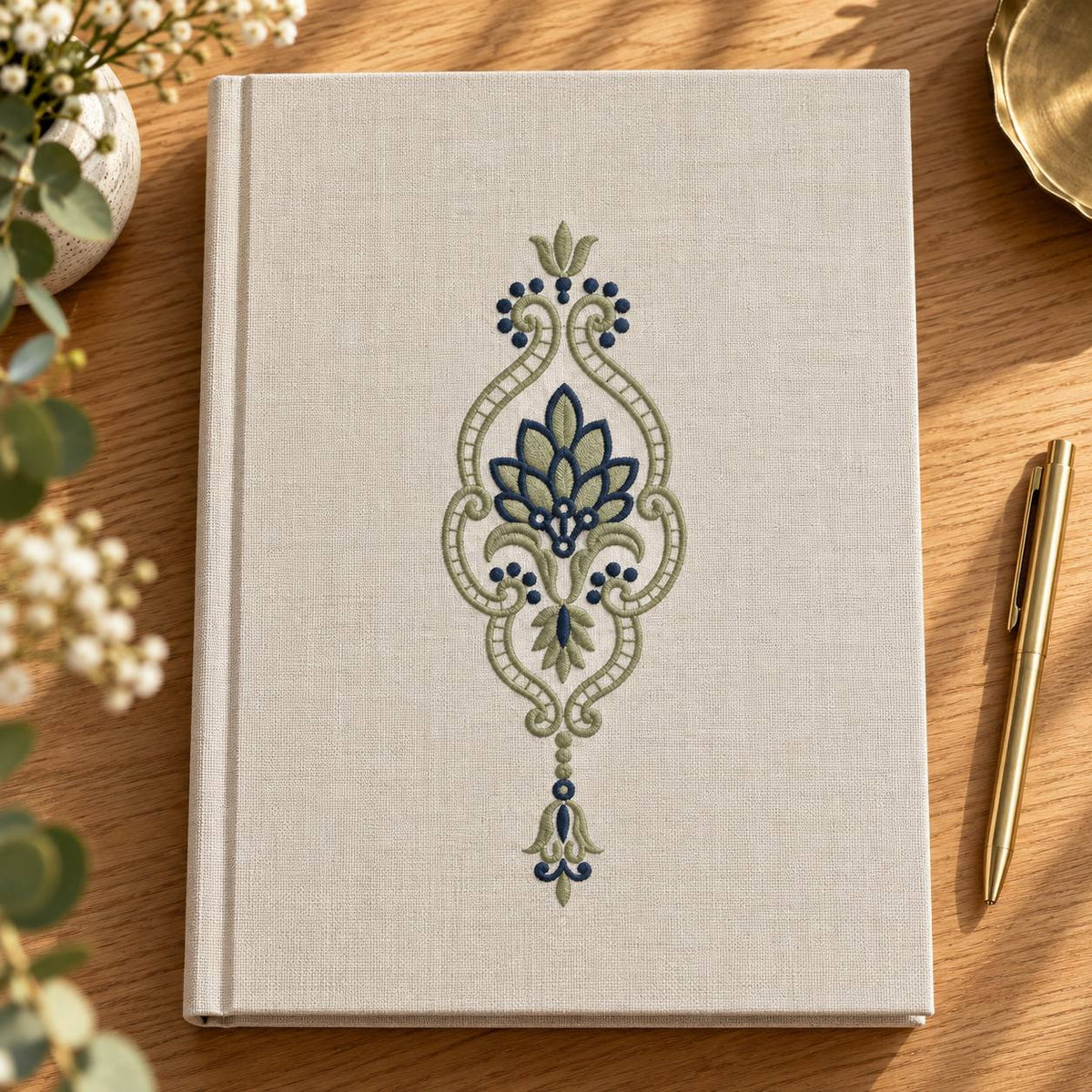 Leaf Fan Scroll Pendant embroidered in smoky sage and ink blue on a linen notebook cover, showing the complete two-color motif.