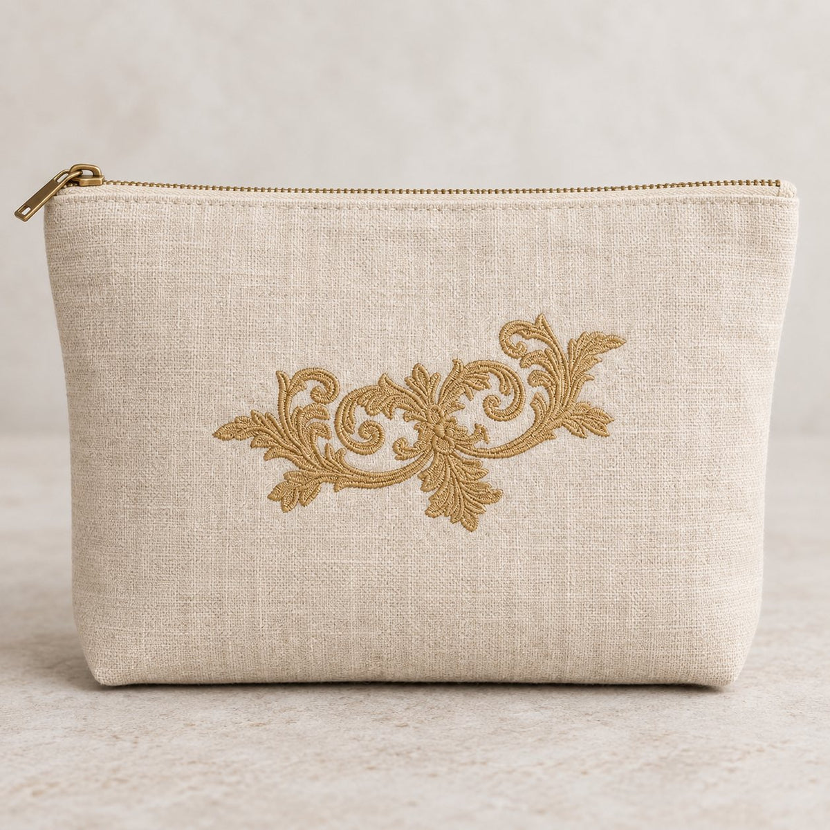 Old-gold floral scroll machine embroidery centered on a natural flax linen zip pouch