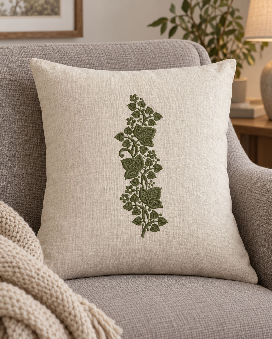 Linen cushion with a single deep muted olive green machine-embroidered ivy leaf and blossom sprig motif on natural ivory linen.