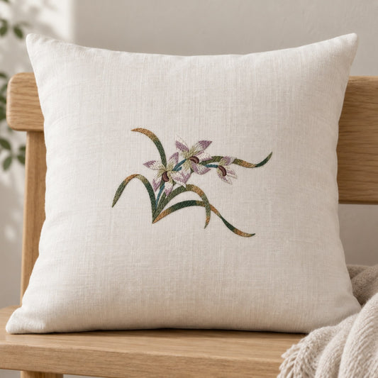 Three orchid flowers and sweeping multitone leaves form a small embroidered spray centered on an ivory cushion.