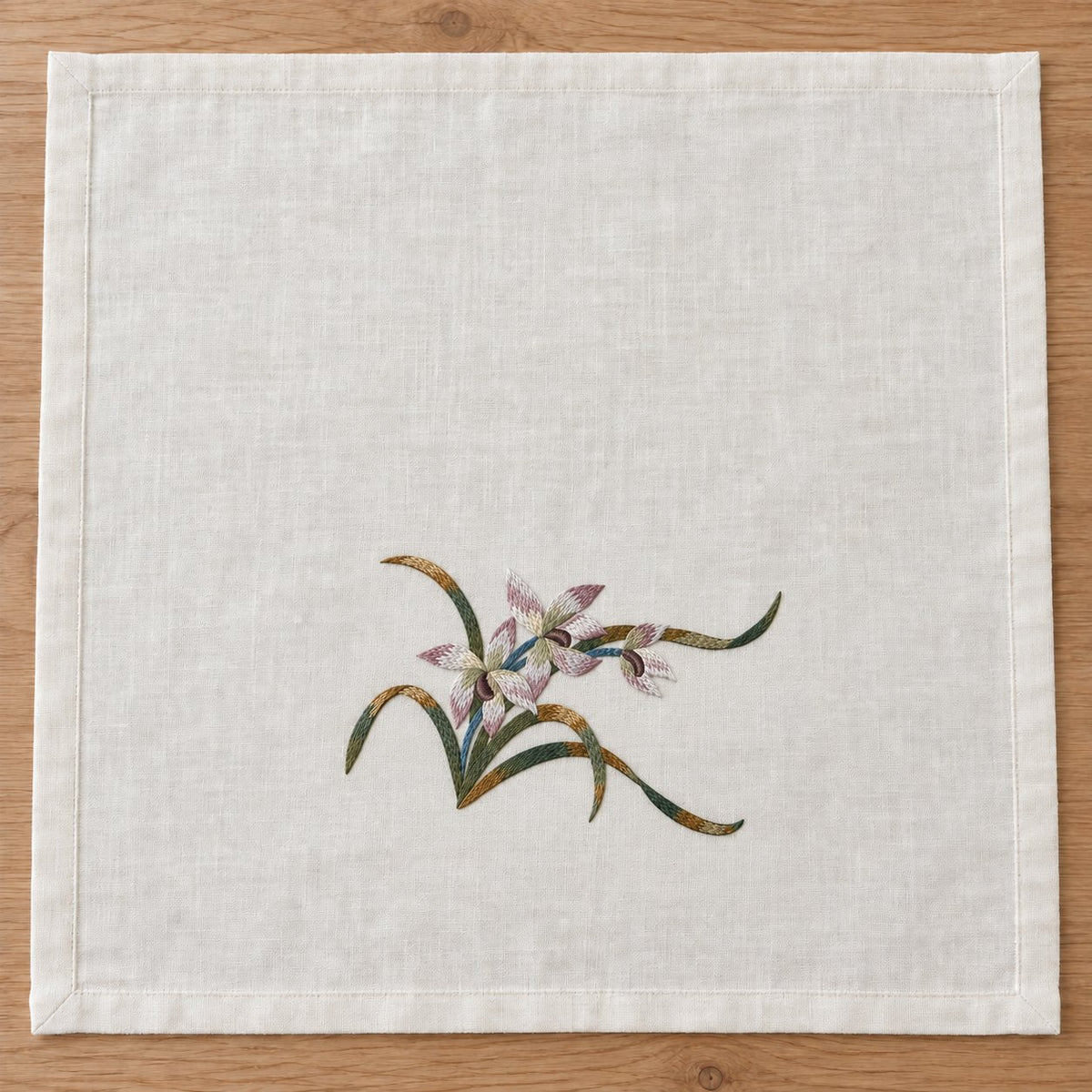 Overhead view of a hemmed ivory linen square with one three-orchid spray positioned near the lower middle.