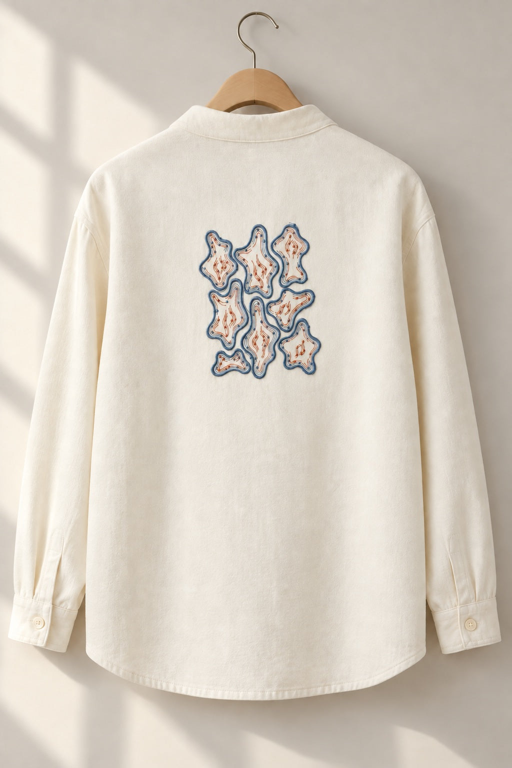 Organic Contour Dot Composition embroidered in smoky indigo and warm terracotta on a cotton overshirt back, showing the complete two-color motif.