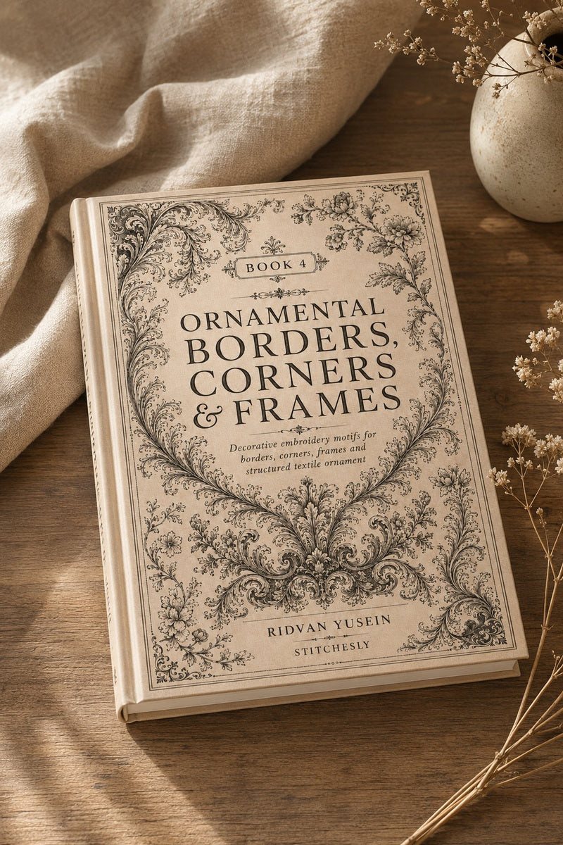 Close view of Ornamental Borders, Corners and Frames, Edition Four cover on ivory linen beside dried botanical sprigs.