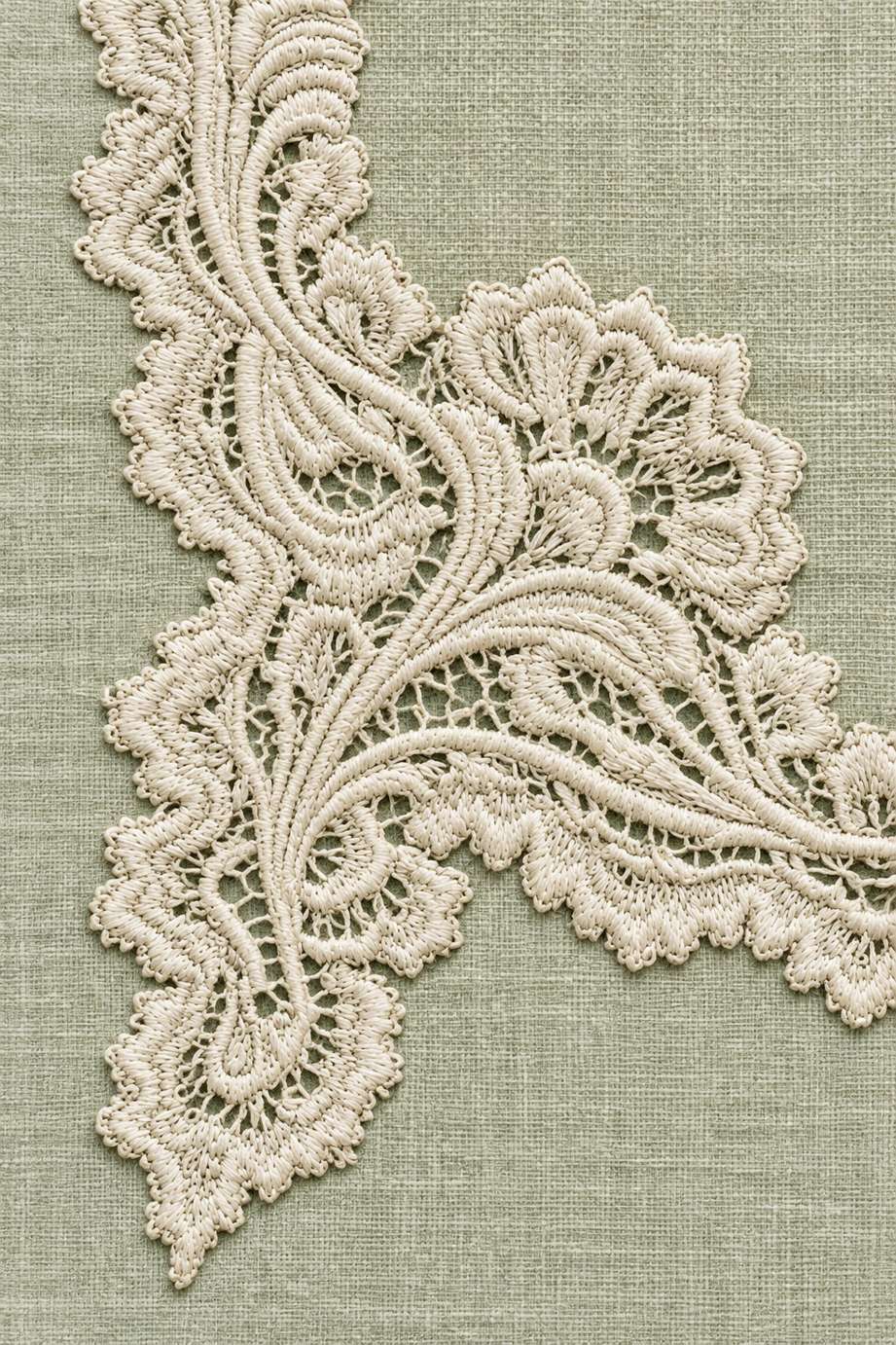 Ivory cotton broderie lace corner with scalloped edges and delicate openwork scrolls on pale celadon linen.