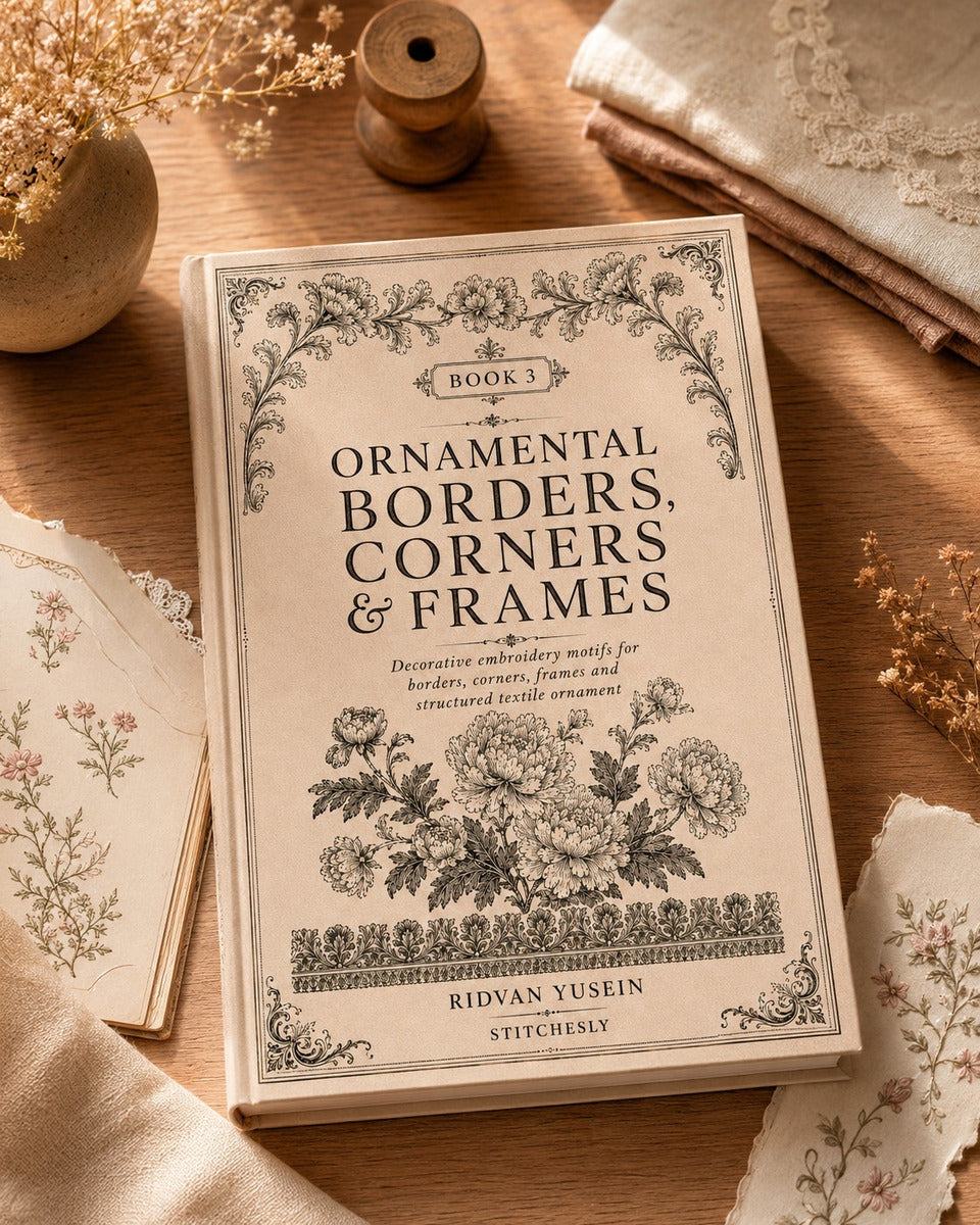 Ornamental Borders, Corners and Frames, Edition Three cover beside a pencil and linen on a wooden desk.