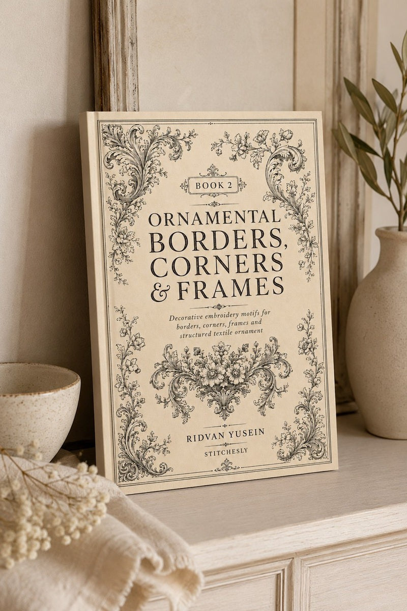 Ornamental Borders, Corners and Frames, Edition Two cover in soft window light beside a ceramic vase.