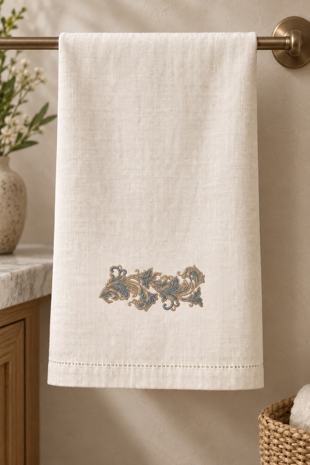 Ivory linen guest towel with a small petrol blue and champagne acanthus scroll above the hem.