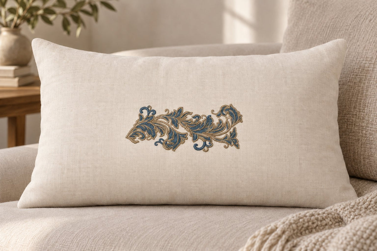 Ivory lumbar cushion featuring one petrol blue and champagne embroidered acanthus scroll in the center.