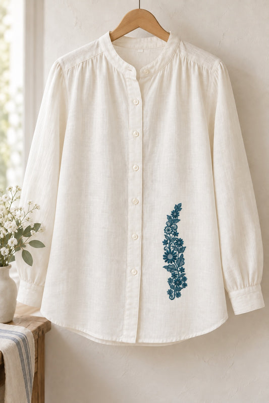Styled linen blouse mockup with a single deep muted petrol teal daisy meadow lace vine embroidered on pale linen; the complete motif has clear fabric around it.