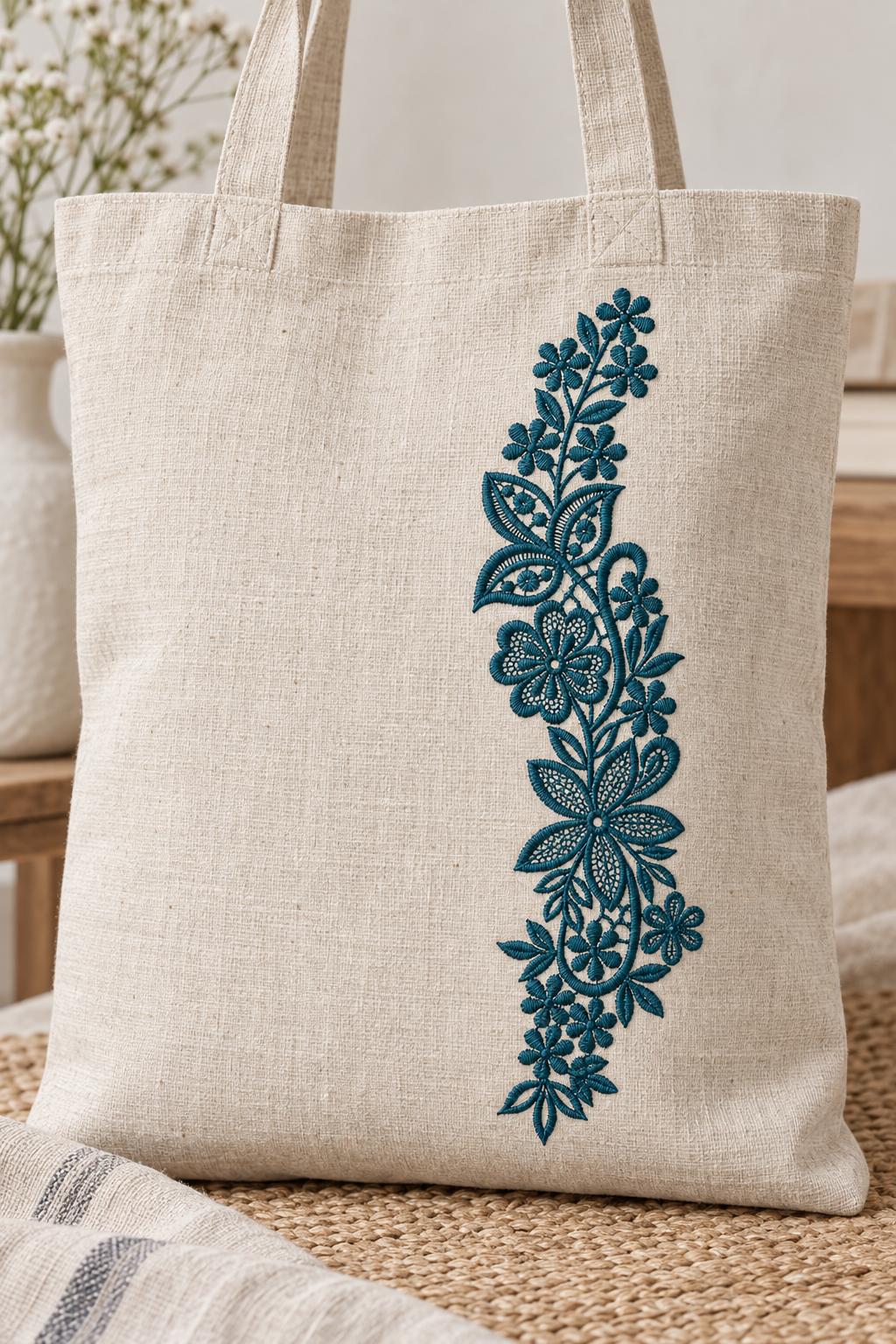 Photorealistic slender floral lace vine machine embroidery in deep petrol teal thread on a natural linen tote bag, shown as one fabric-stitched motif