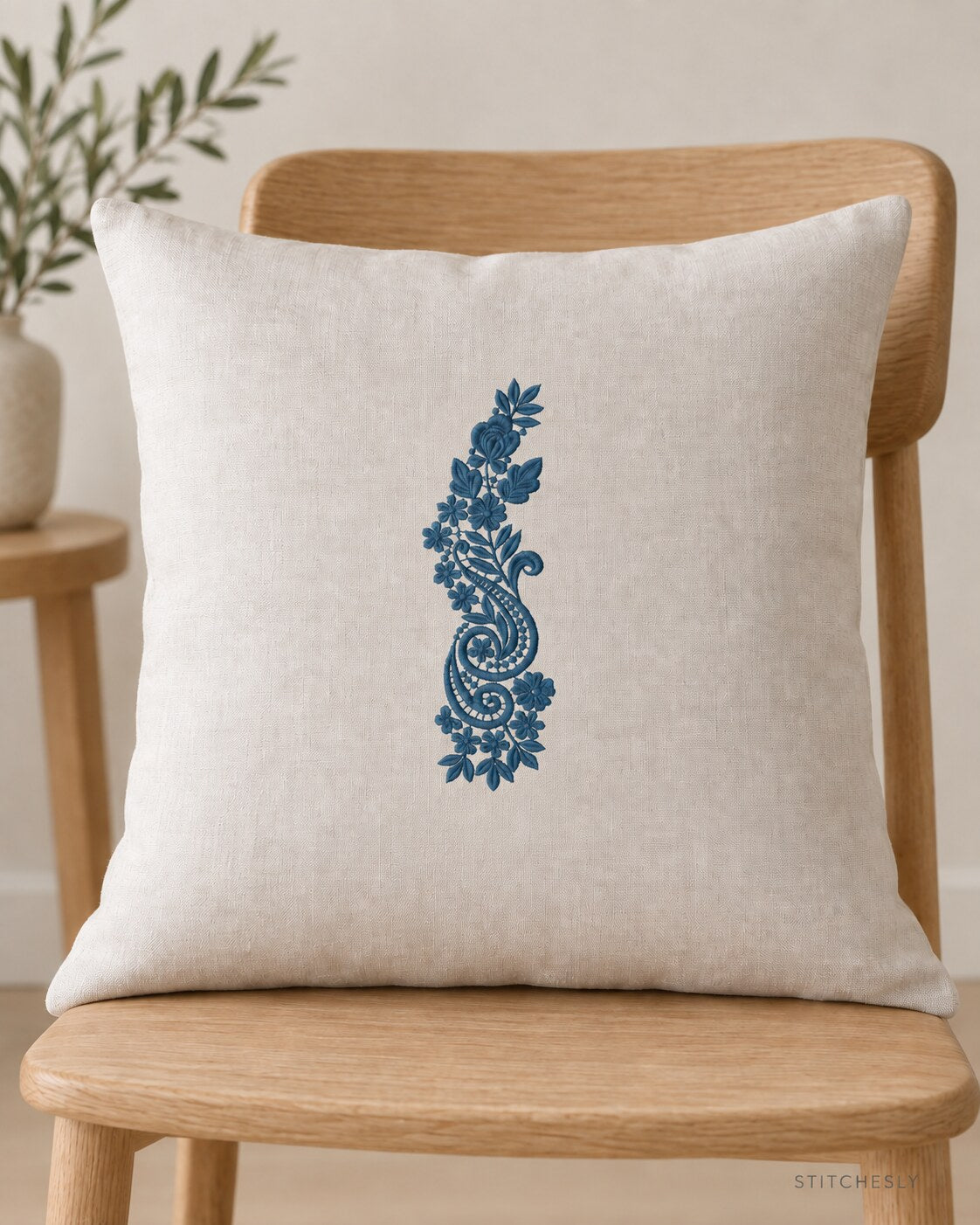 Generated usage mockup of a linen cushion with the rose and twin paisley spray machine embroidery motif in one deep muted petrol blue thread color.