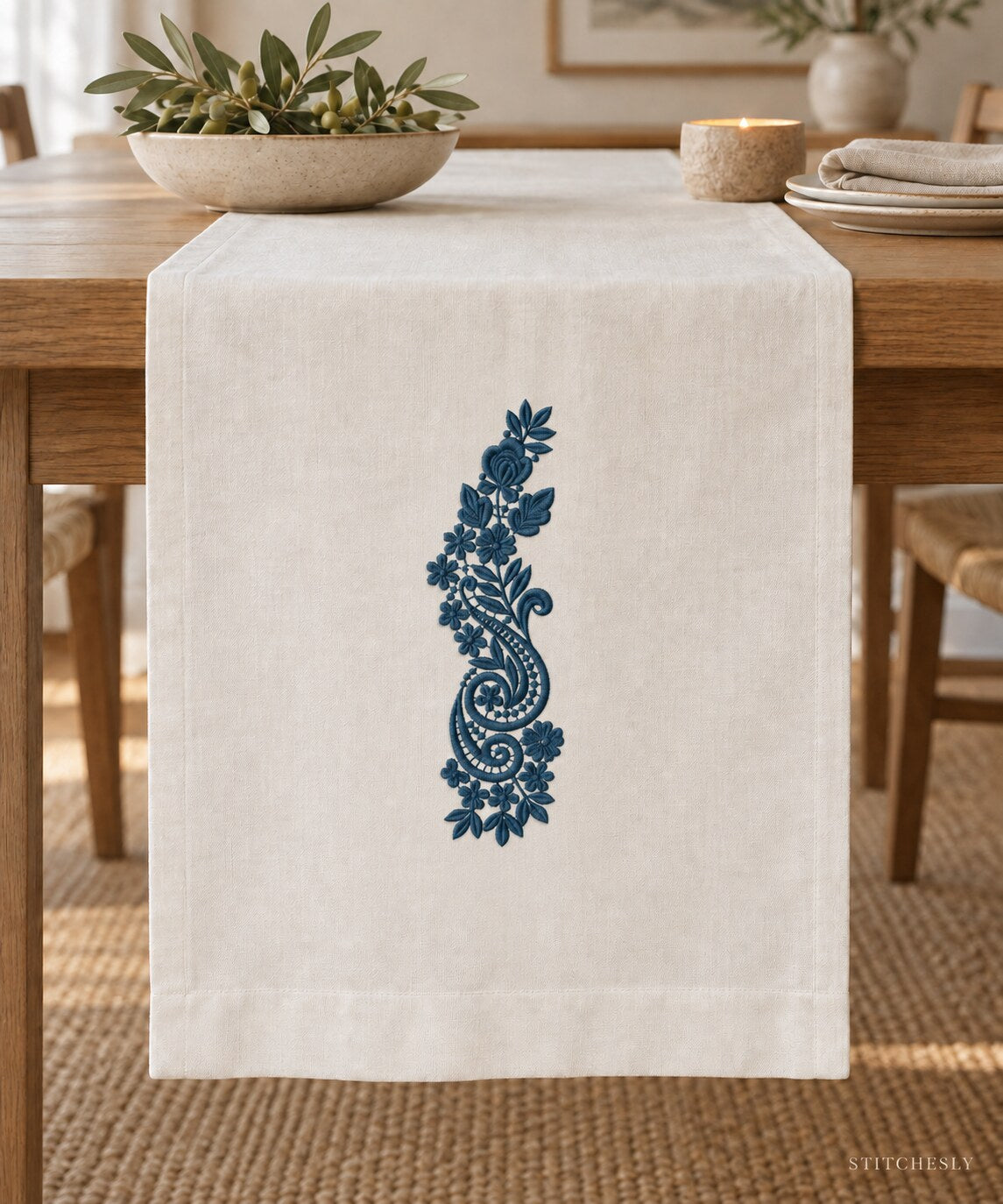 Generated usage mockup of a linen table runner with the rose and twin paisley spray machine embroidery motif in one deep muted petrol blue thread color.