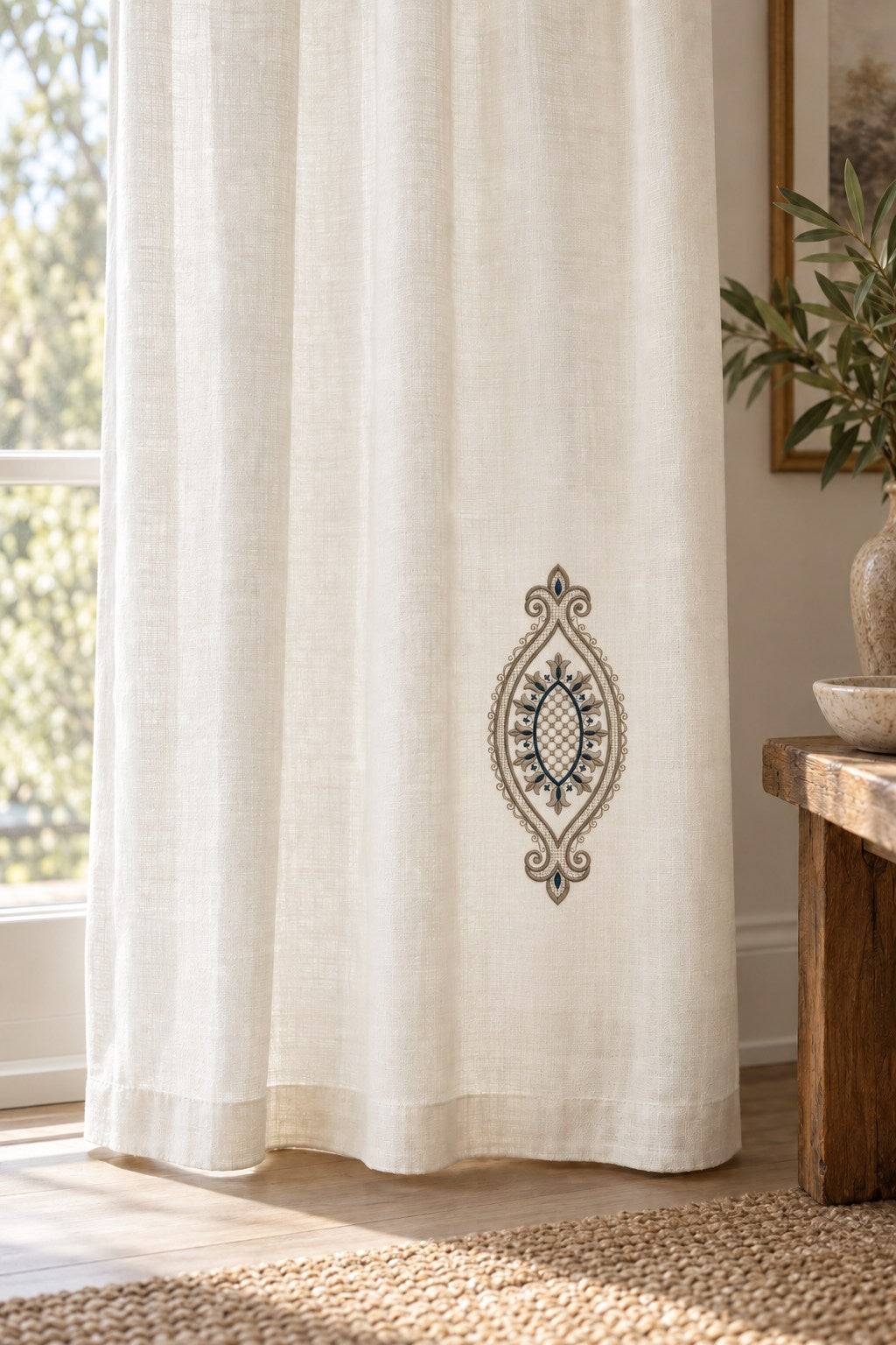 Ivory linen curtain with a single small-looking vertical medallion near the lower inside edge.