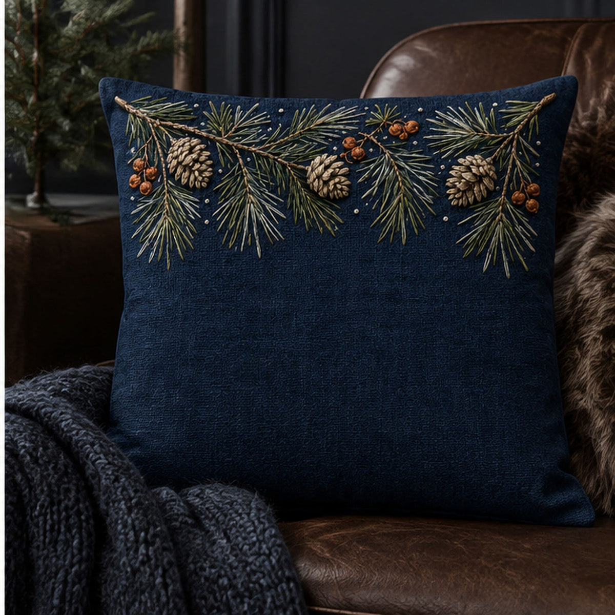 Navy linen cushion mockup featuring the Pine Needle Top Border hand embroidery design. Pine boughs, cones and rust berries gather along the top edge of the drawing.