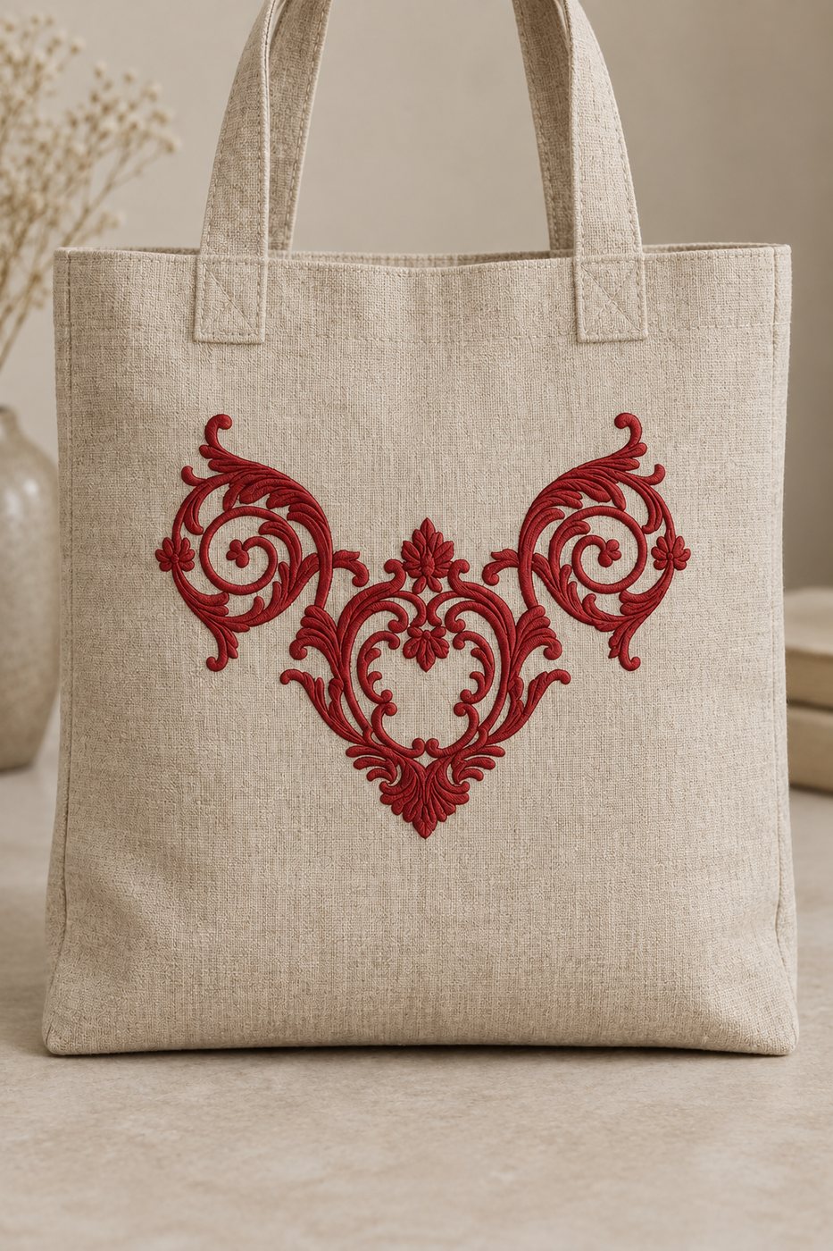 Pomegranate red ornamental scroll crest machine embroidery centered on a natural linen tote