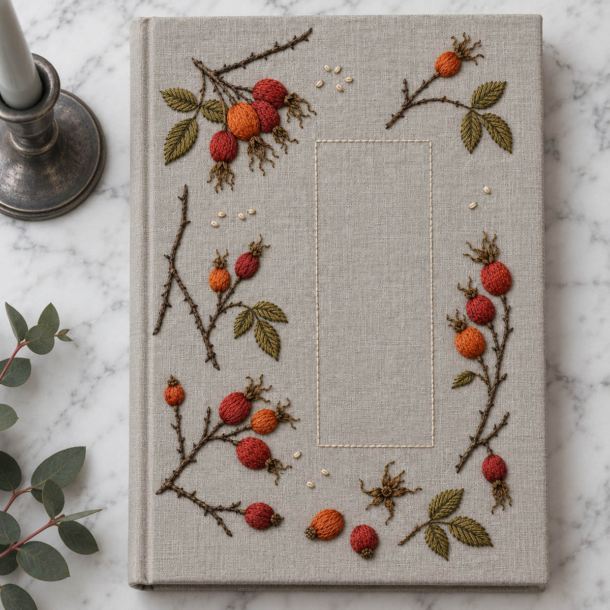 Linen notebook cover mockup featuring the Rosehip Winter Scatter hand embroidery design. Rosehip branch fragments sit around a tall rectangle of clear linen.