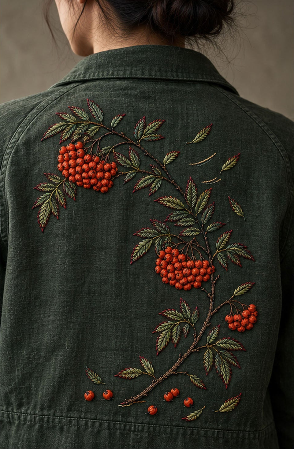Green linen jacket mockup featuring the Rowan Berry Arc hand embroidery design. Coral rowan berries follow a broken diagonal branch on moss-coloured linen.