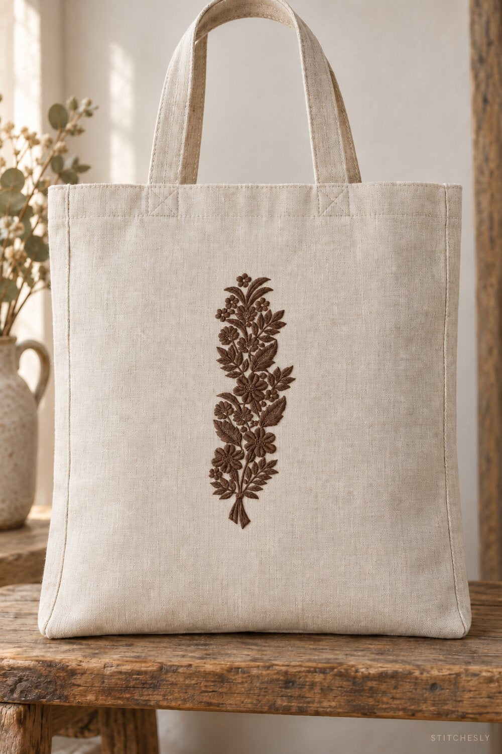 Generated usage mockup of a linen tote bag with the ribbon tied meadow bouquet machine embroidery motif in one rich muted dark sepia brown thread color.
