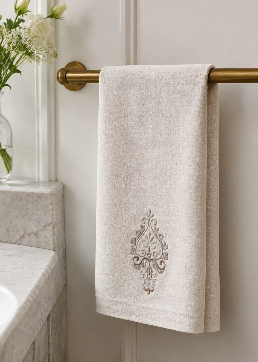Compact silver damask teardrop machine embroidery design stitched near the hem of an ivory linen guest towel