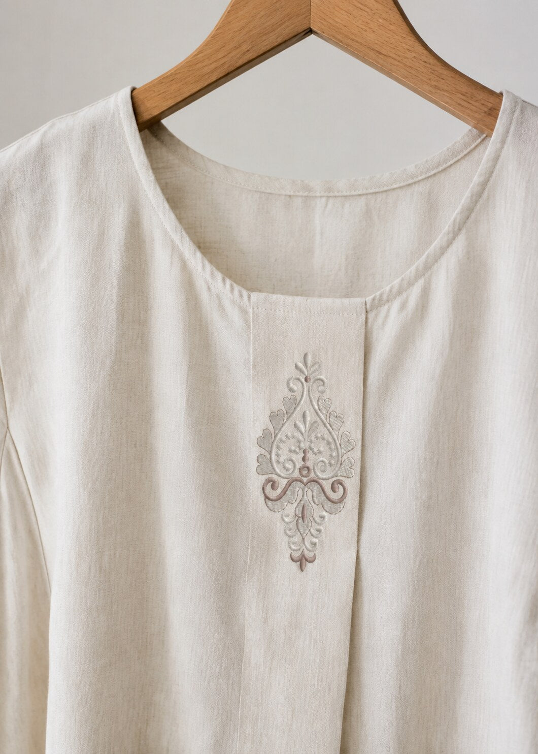 Compact silver damask teardrop embroidery placed vertically on the front placket of an ivory linen blouse
