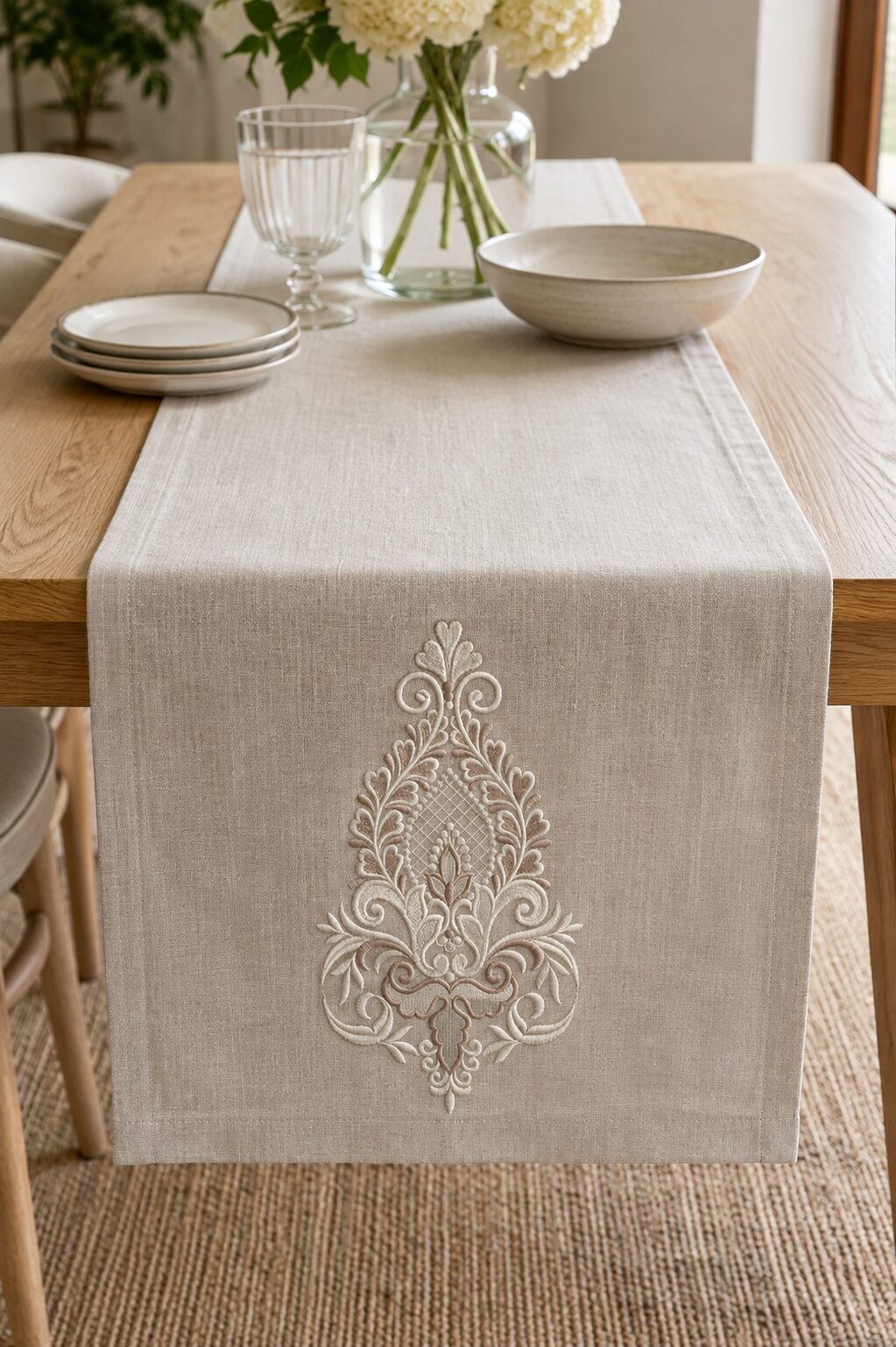 Large silver damask teardrop embroidery displayed at the end of a natural linen table runner on a pale oak dining table