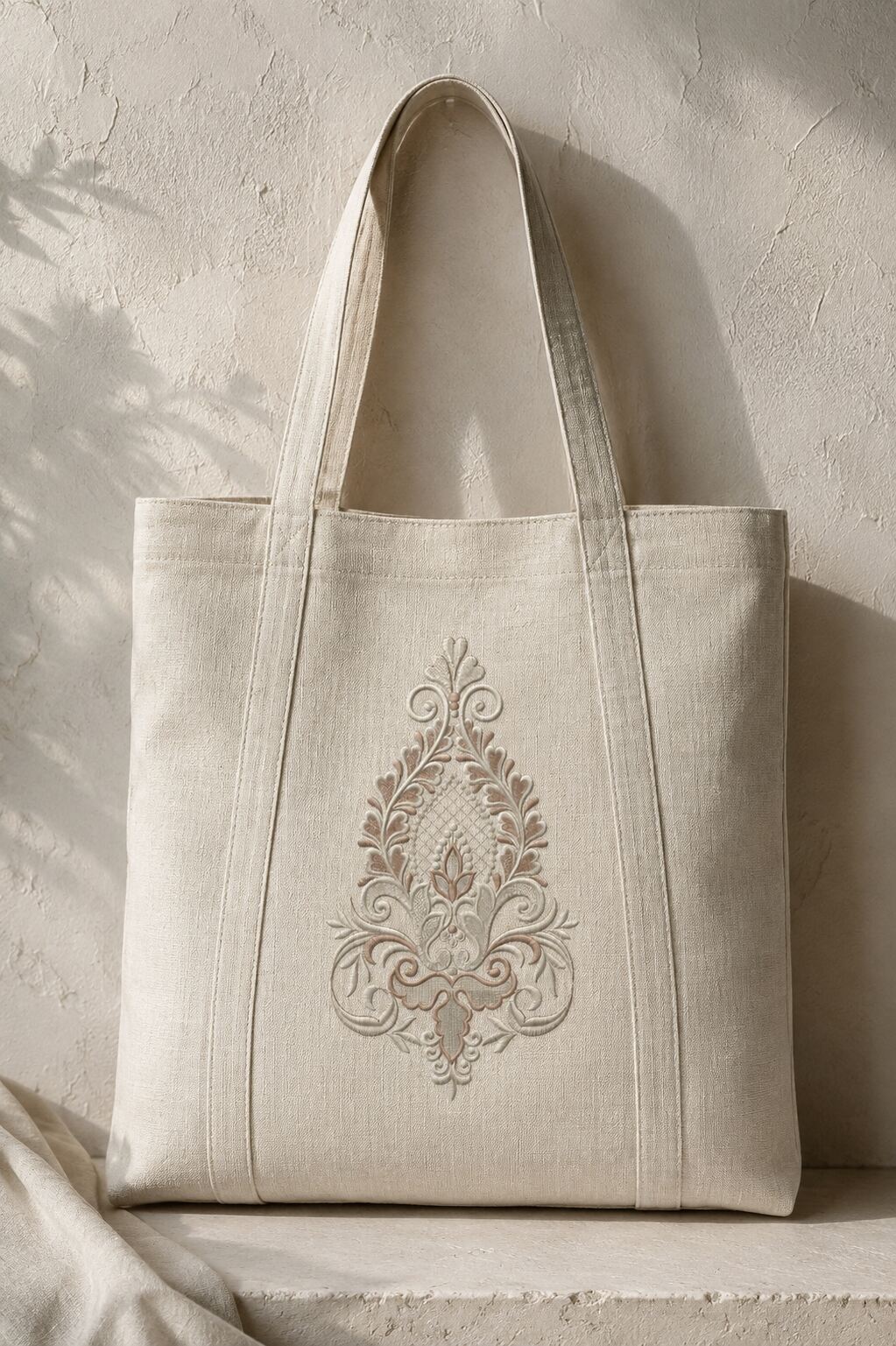 Large taupe and ivory damask machine embroidery design centered on a structured natural linen tote bag