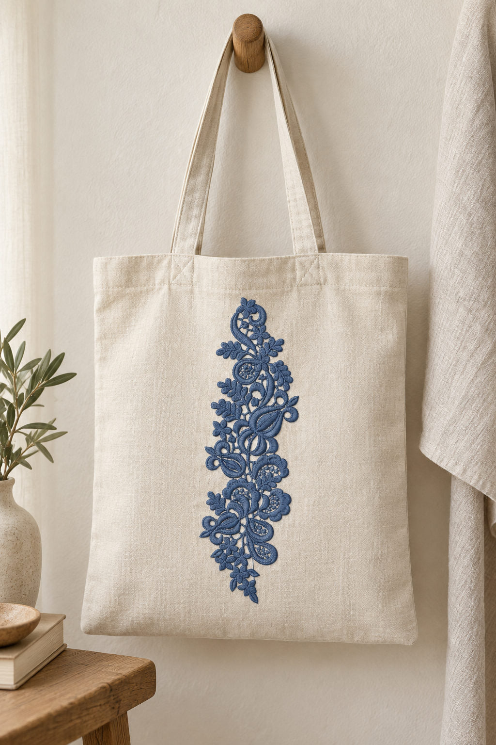Linen tote bag with a single deep slate blue machine-embroidered paisley lace botanical spray motif on natural ivory linen.