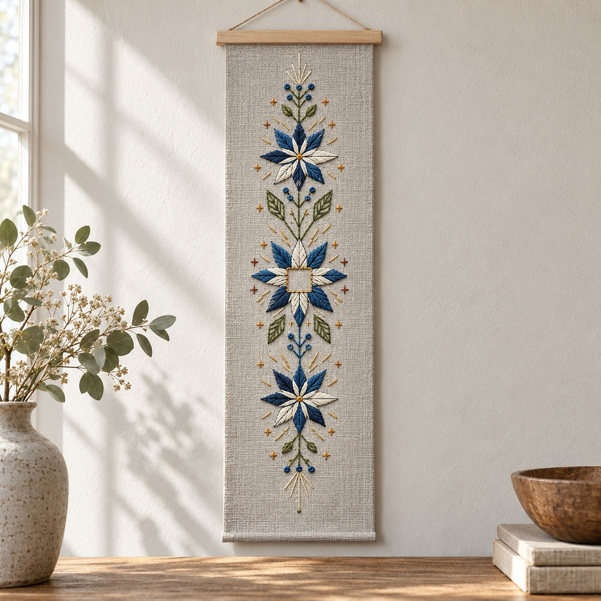 Hanging snowflower panel mockup featuring the Snowflower Center Panel hand embroidery design. Blue-white snowflowers form a narrow vertical arrangement around an unfilled square detail.