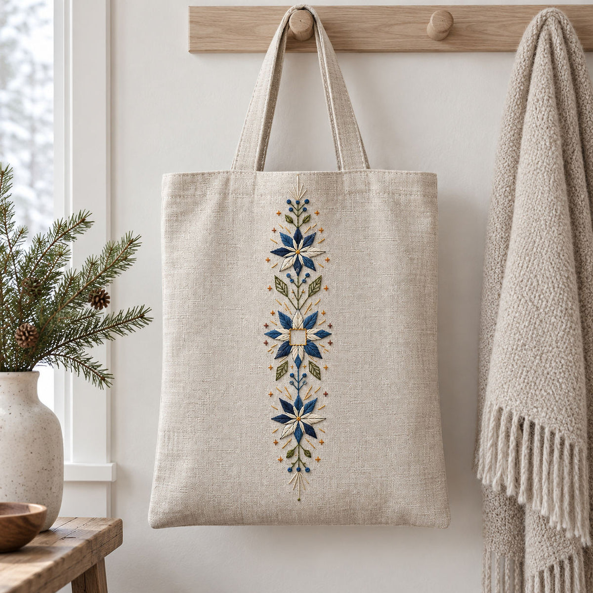 Linen tote bag mockup featuring the Snowflower Center Panel hand embroidery design. Blue-white snowflowers form a narrow vertical arrangement around an unfilled square detail.