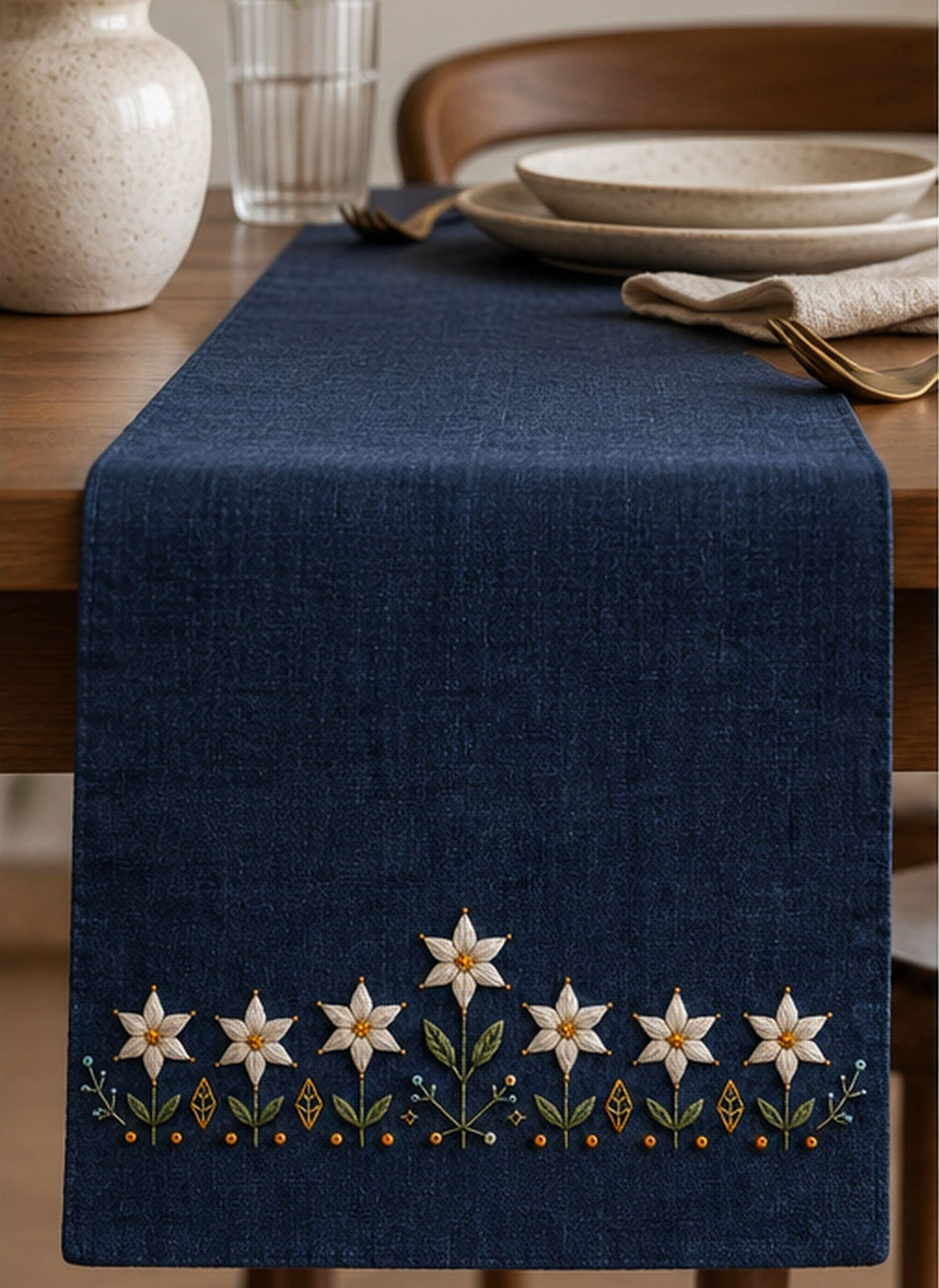 Navy linen apron mockup featuring the Starflower Border Chain hand embroidery design. White starflowers form a low border on indigo, with a taller central bloom and small geometric ground marks.