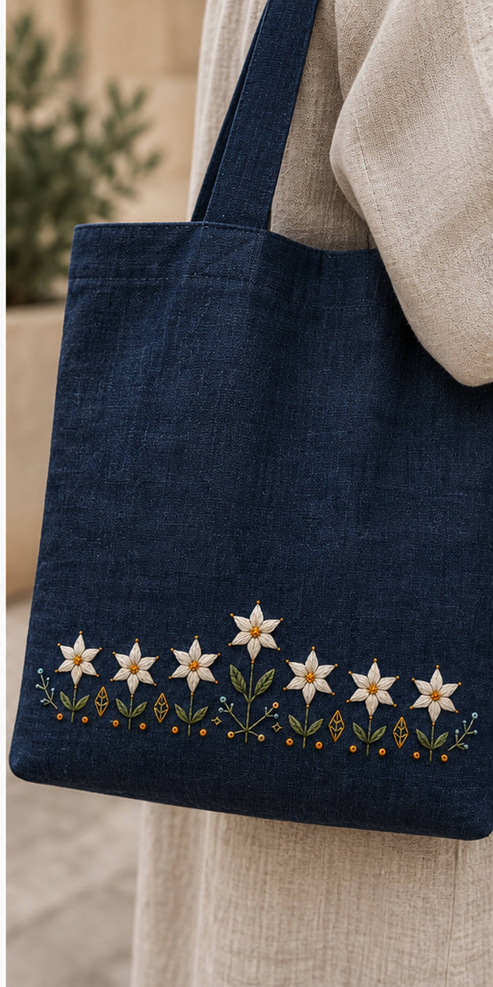 Navy linen tote bag mockup featuring the Starflower Border Chain hand embroidery design. White starflowers form a low border on indigo, with a taller central bloom and small geometric ground marks.