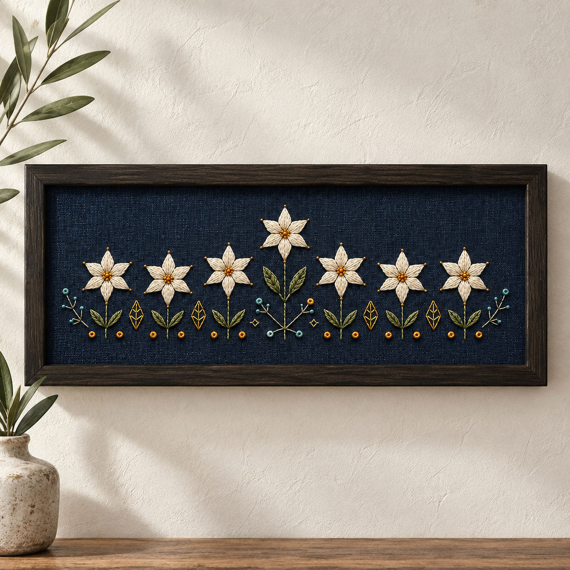 Framed navy textile mockup featuring the Starflower Border Chain hand embroidery design. White starflowers form a low border on indigo, with a taller central bloom and small geometric ground marks.