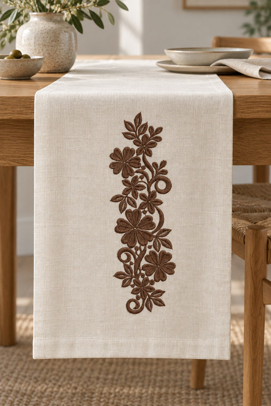 Linen table runner with a single rich muted walnut brown machine-embroidered heart petal floral scroll motif on natural ivory linen.