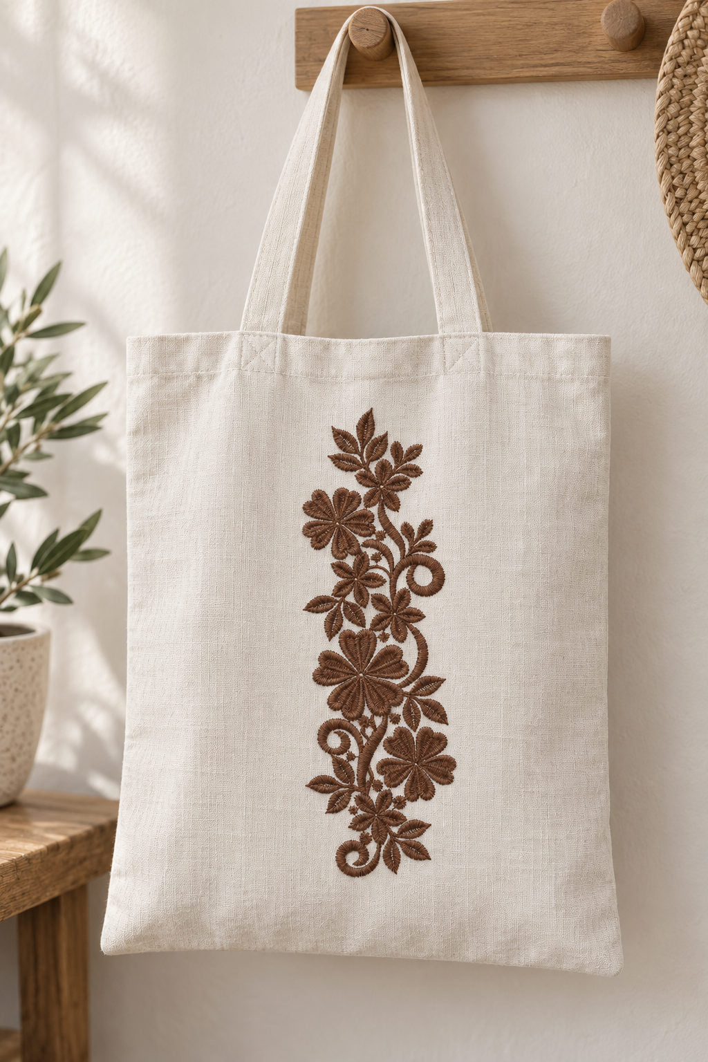 Linen tote bag with a single rich muted walnut brown machine-embroidered heart petal floral scroll motif on natural ivory linen.