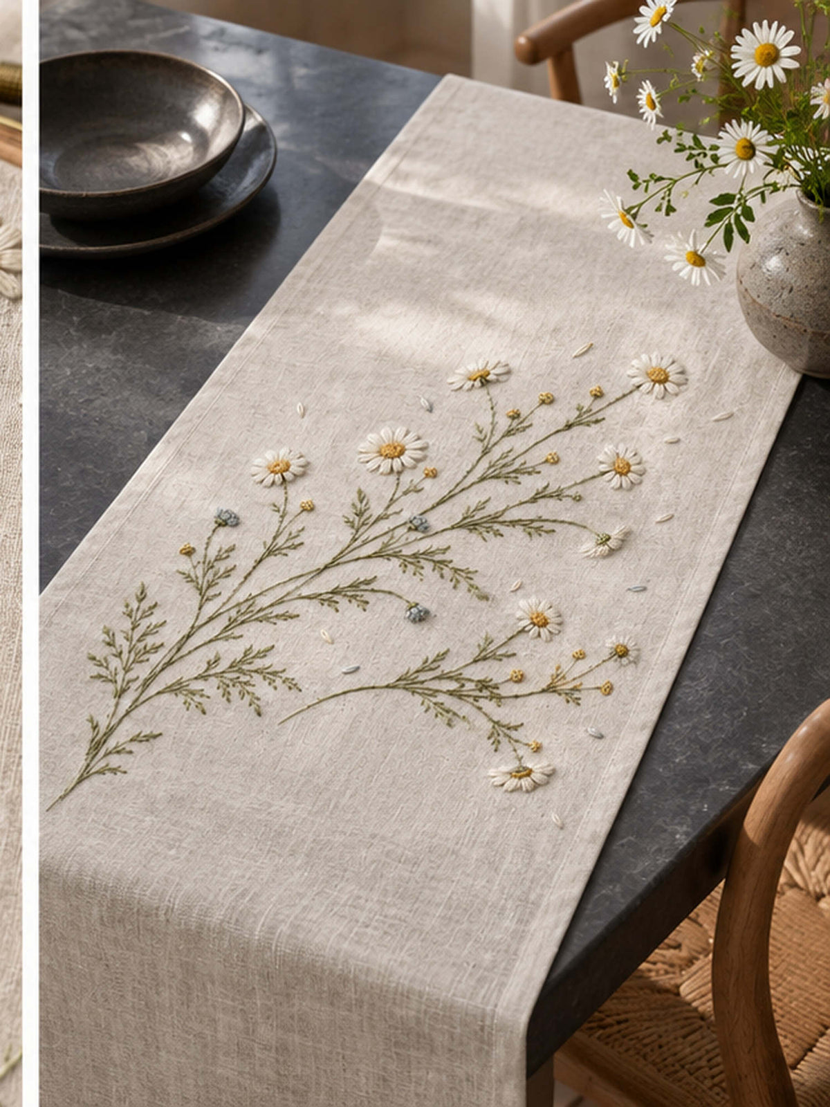 Linen runner on a table mockup featuring the Wild Chamomile Drift hand embroidery design. White chamomile heads, golden centres and fine olive foliage spread across the linen in a loose drift.