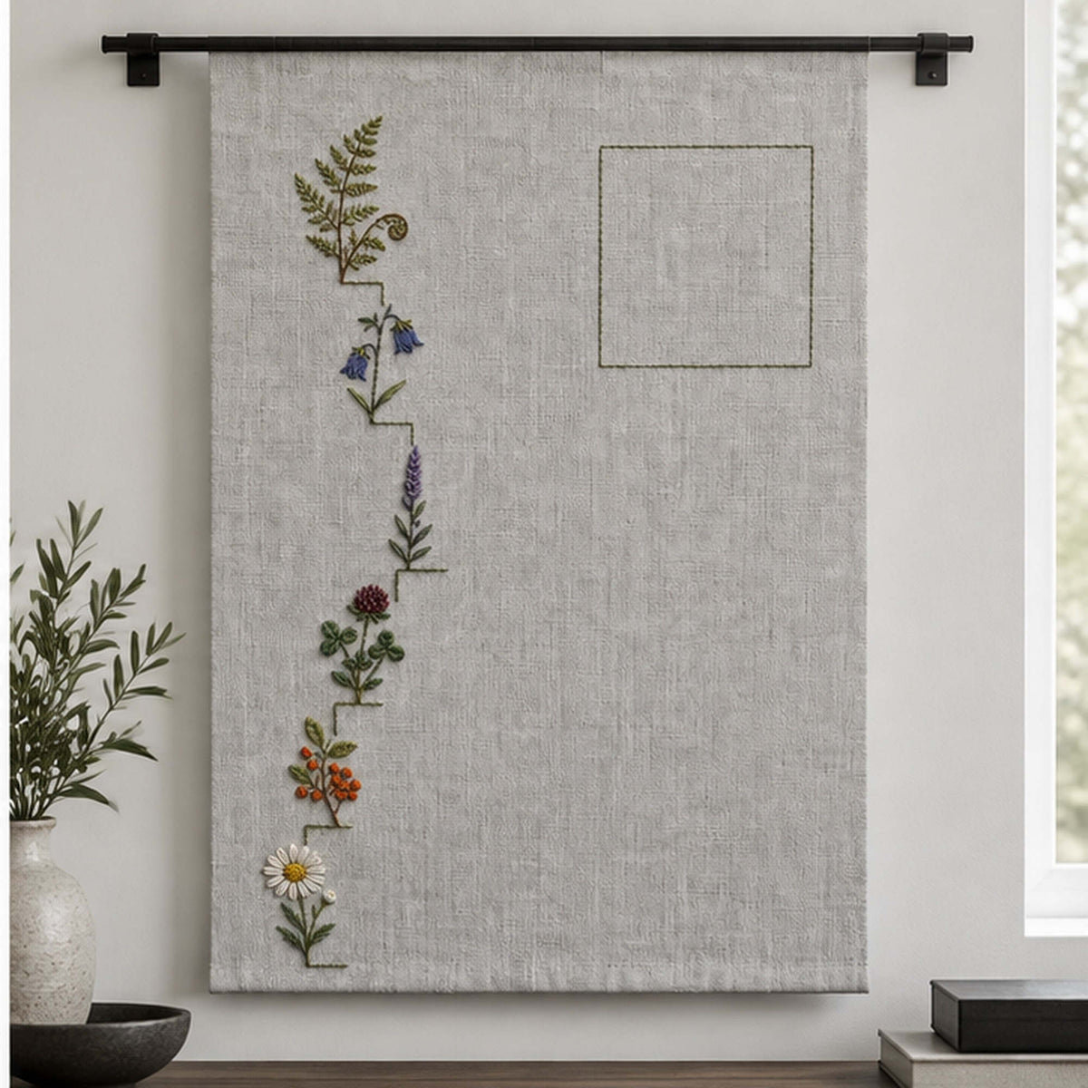 Hanging linen panel mockup featuring the Wildflower Stair Border hand embroidery design. Wildflowers climb a stepped left border beside an outlined area of clear linen.