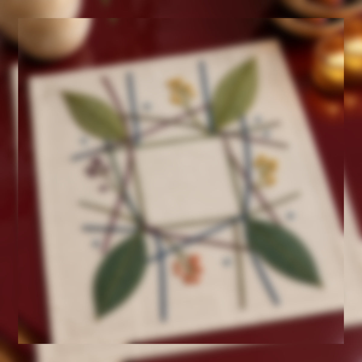 Close view of the leaf grid mockup featuring the Woven Leaf Grid hand embroidery design. Cool blue and pine-green leaf stems cross an open woven grid.